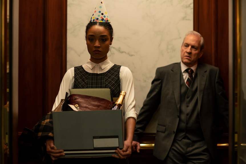 A Black woman in her late 20s in a party hat and holding a box of stuff, sad, in a lift with an old white man