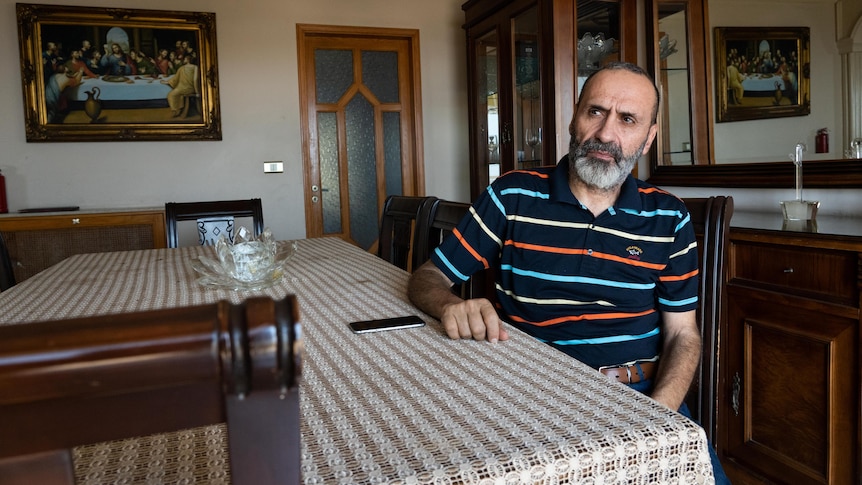 A middle-aged bearded Lebanese man in a polo shirt sits at a dining room table 