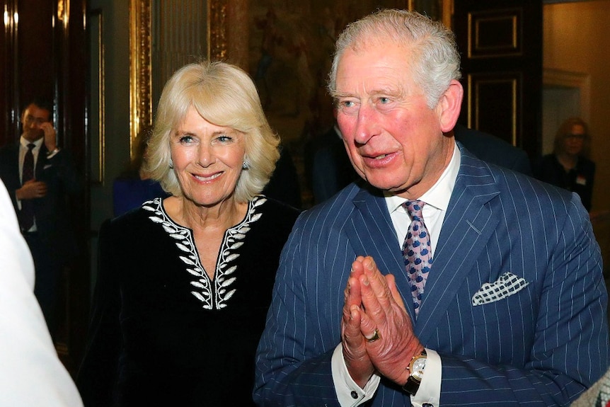 Britain's Prince Charles and Camilla entering a hall speaking to another person.