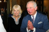 Britain's Prince Charles and Camilla entering a hall speaking to another person.