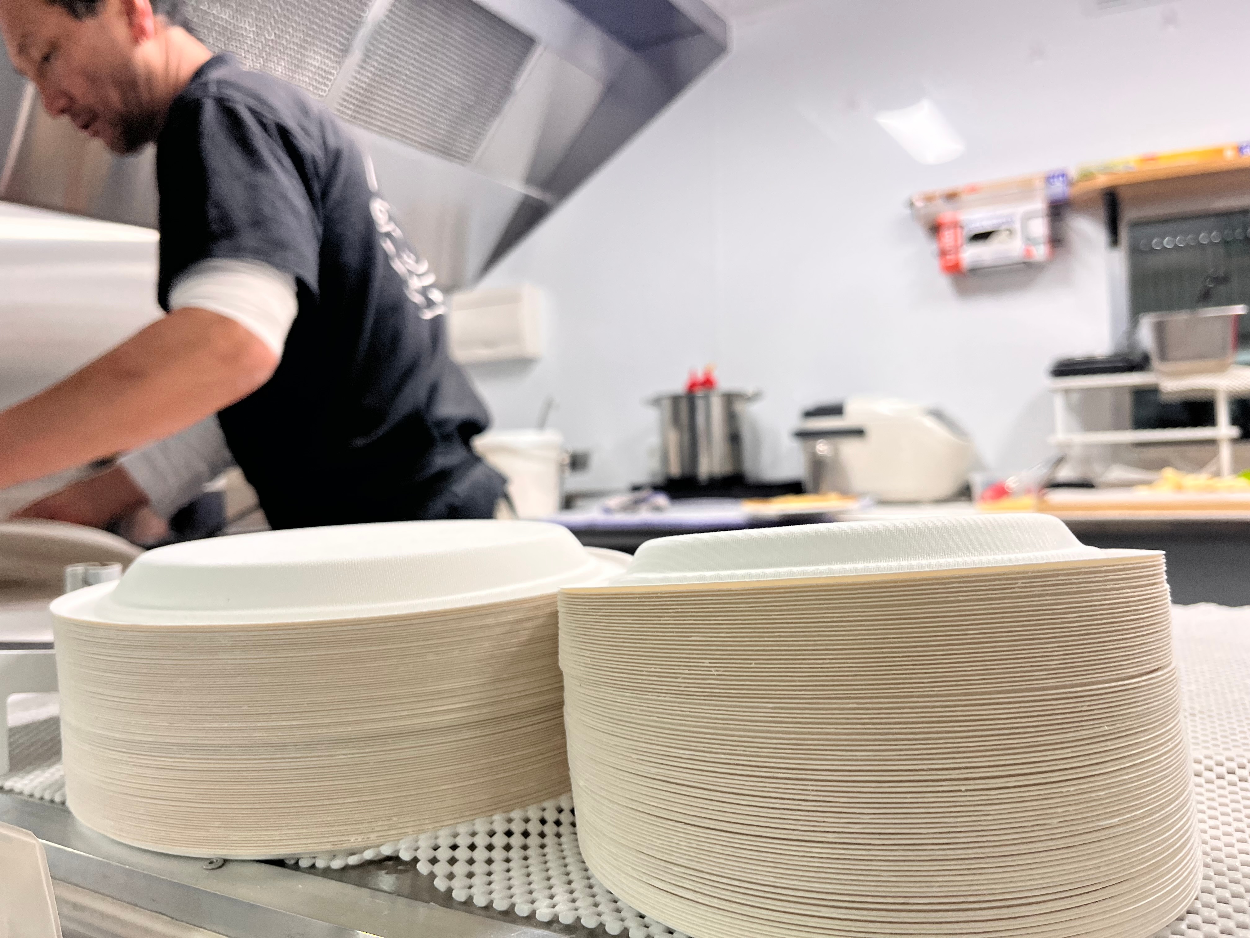 Two stacks of paper plates on a bench in an industrial kitchen.