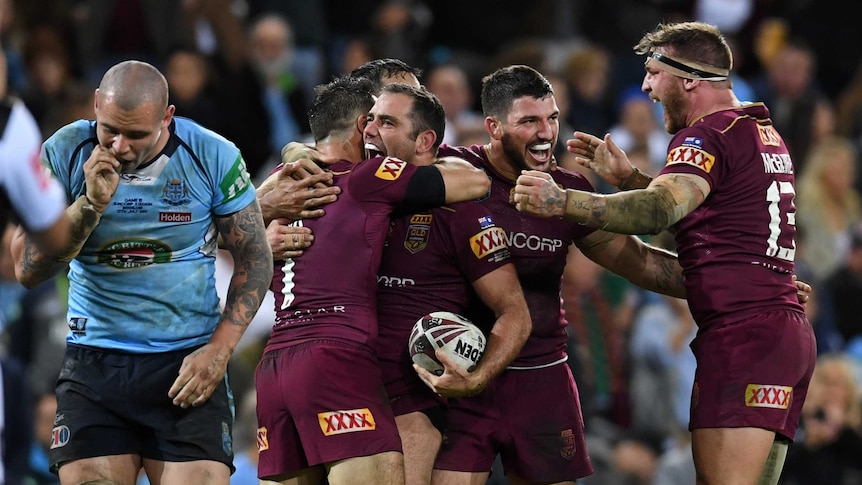 Cameron Smith and Cooper Cronk hug each other with team-mates around after Queensland won State of Origin III.