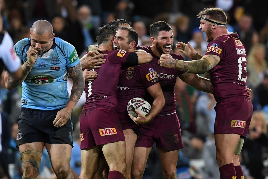 Cameron Smith and Cooper Cronk hug each other with team-mates around after Queensland won State of Origin III.