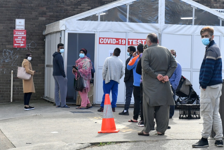 people wearing masks outside a tent set up to be a testing clinic