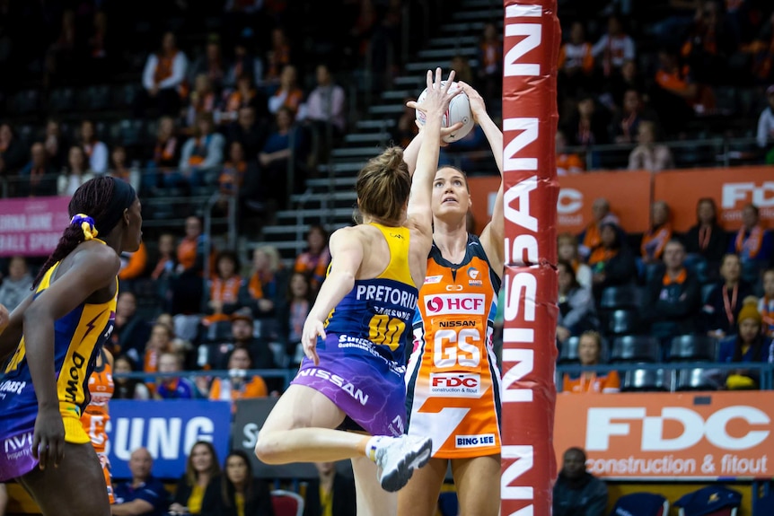 A netball player takes a shot at goal from under the ring.