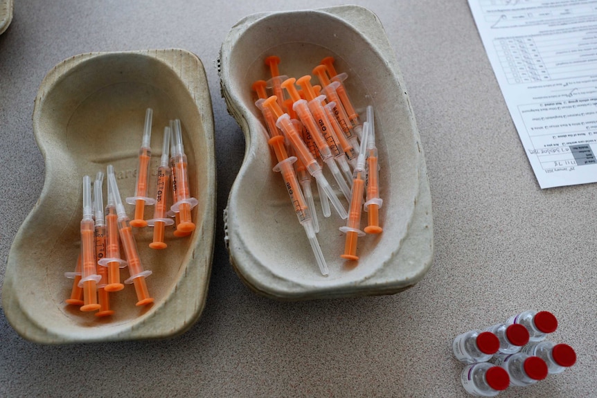 Vials of the AstraZeneca vaccine and loaded syringes sit in two trays