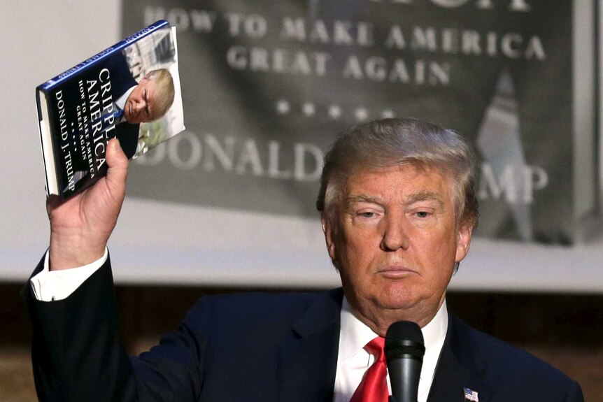 Donald Trump holds aloft a copy of his book, Crippled America