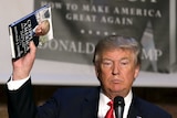 Donald Trump holds aloft a copy of his book, Crippled America