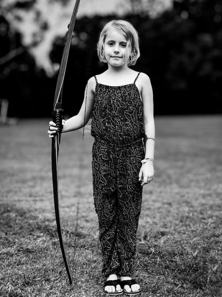A young girl holding a longbow in a black and white shot
