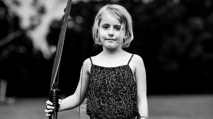 A young girl holding a longbow in a black and white shot