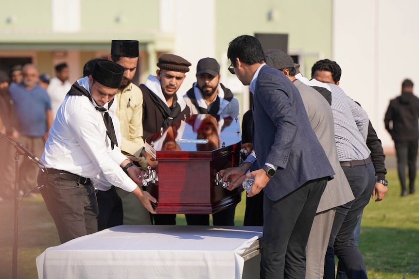 A number of men carry a casket outside a mosque.