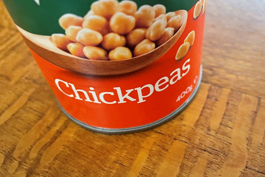 Close up of a can of chickpeas on a silky oak surface. 