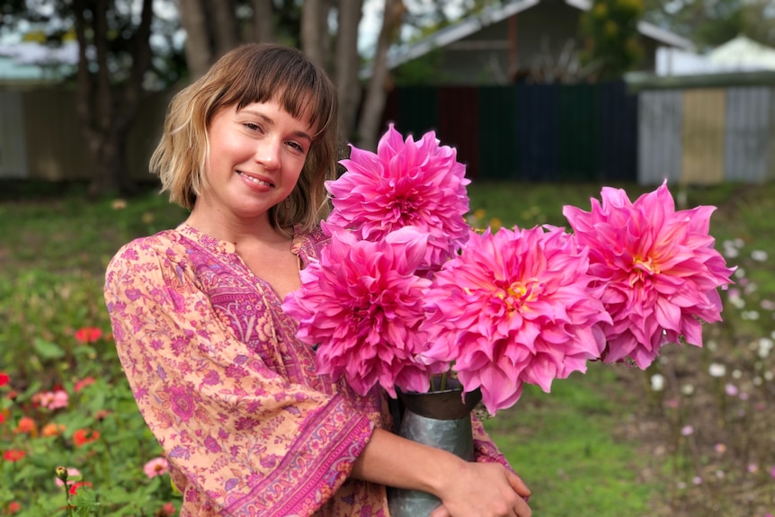A woman holds a big bunch of bright pink flowers.
