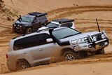 A four-wheel drive goes through dunes at Stockton beach - two other four-wheel drives are behind the car. 
