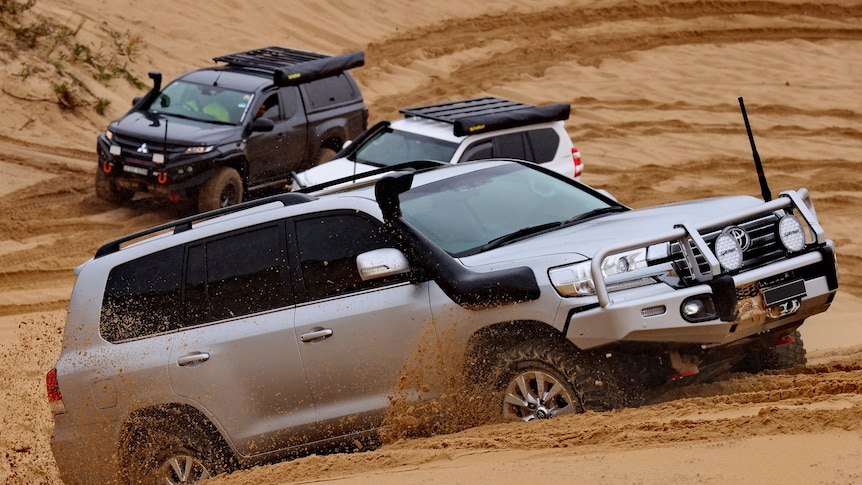 A four-wheel drive goes through dunes at Stockton beach - two other four-wheel drives are behind the car. 