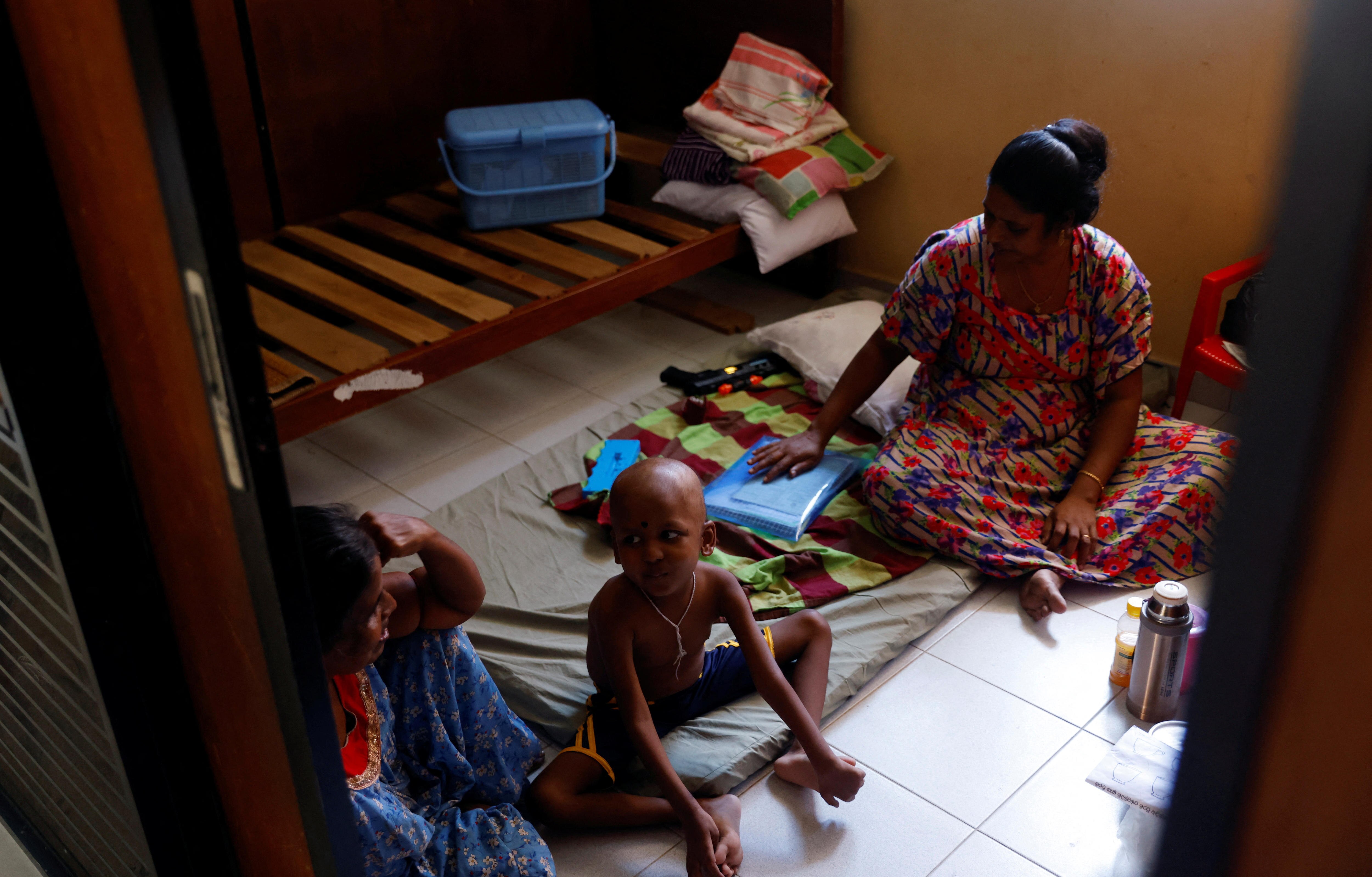 two women sit on the floor with a young boy near a bed in a room
