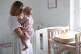 Woman holds her baby closely and smiles while standing in the baby's room.