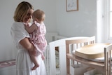 Woman holds her baby closely and smiles while standing in the baby's room.