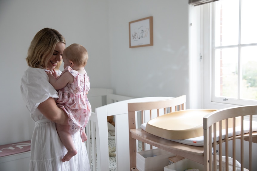 Woman holds her baby closely and smiles while standing in the baby's room.