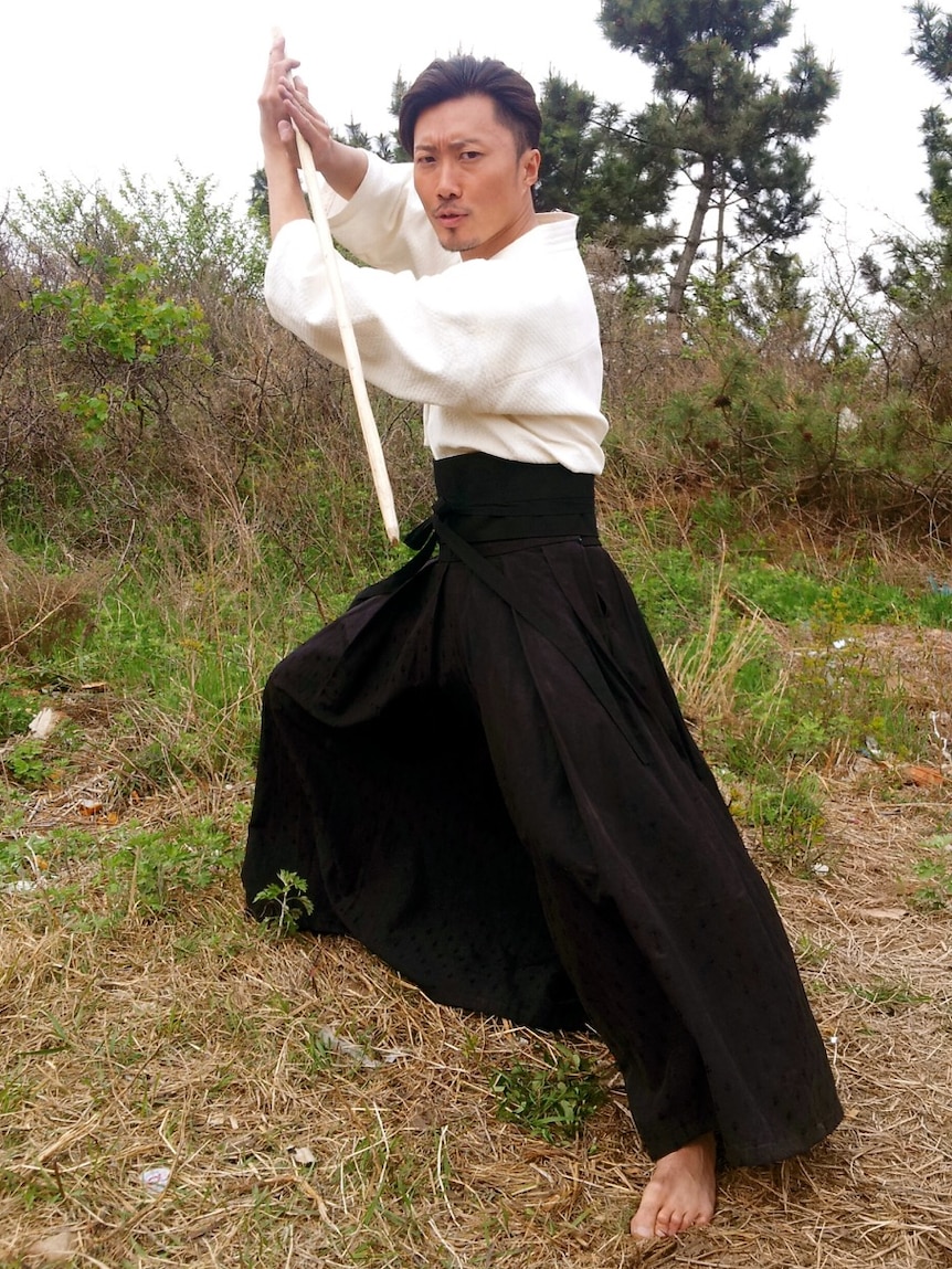 A man in Japanese traditional dress brandishing a fighting stick
