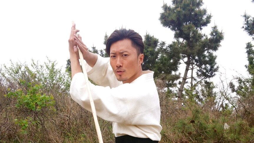 A man in Japanese traditional dress brandishing a fighting stick