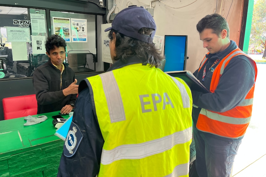 A man talks to two men who are wearing high-vis vests.