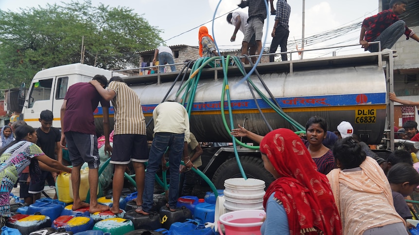 People climbing on top and standing on blue barrels and a truck with hoses down the side 
