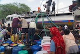 People climbing on top and standing on blue barrels and a truck with hoses down the side 