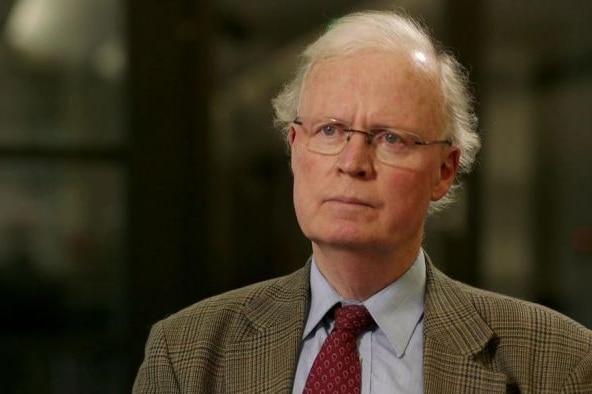 A man looking serious and wearing a tweed suit and a red tie.