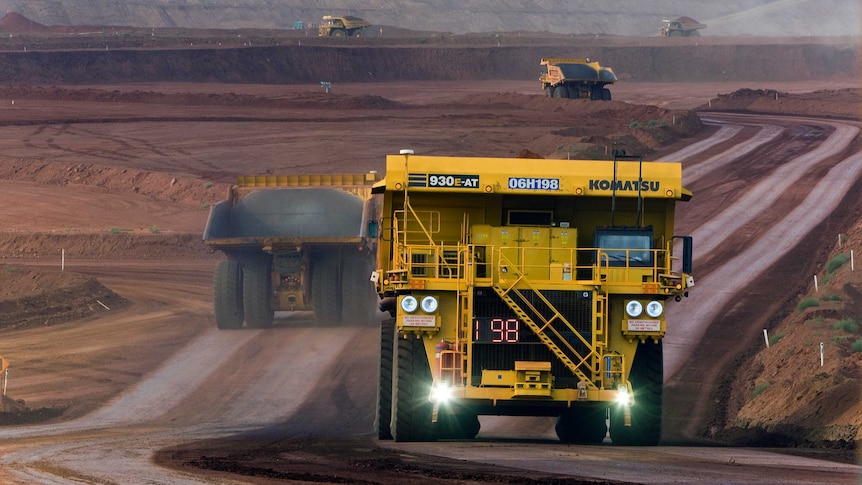 A large yellow autonomous haul truck drives along a dirt road at a mine in the Pilbara.