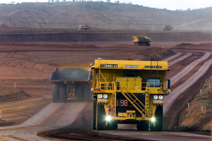 A large yellow autonomous haul truck drives along a dirt road at a mine in the Pilbara.