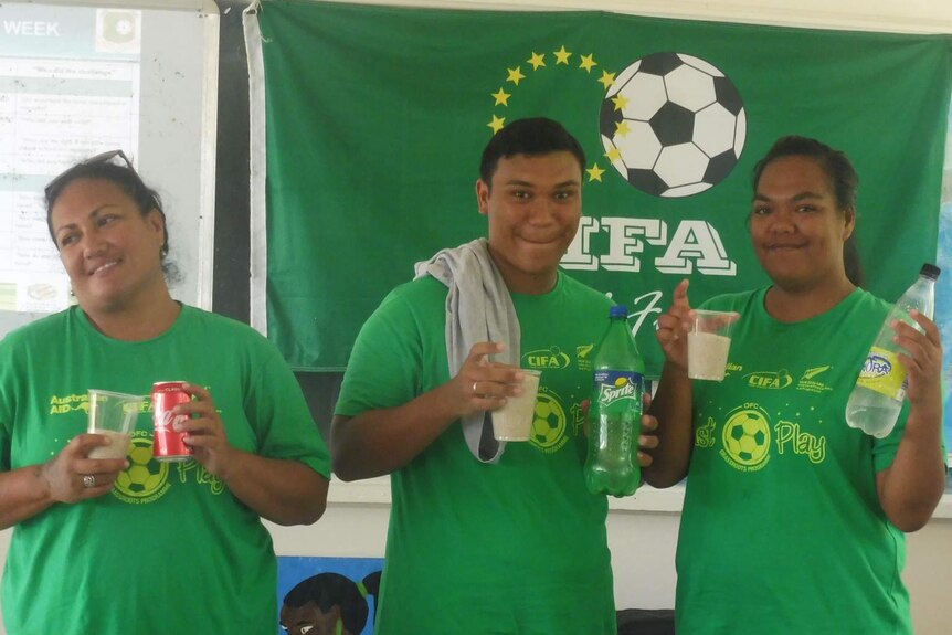 Three adults hold cans and bottles of soft drinks next to the amount of sugar that is in each of them