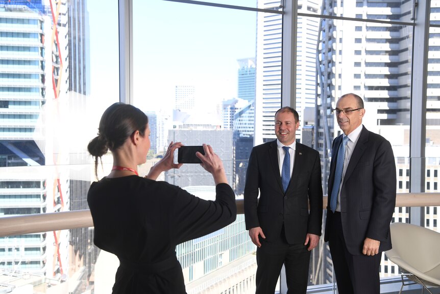 a woman taking a photo of two men in suits in an office building
