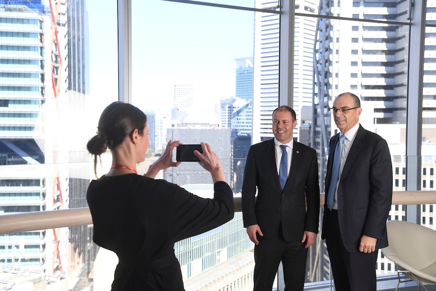 a woman taking a photo of two men in suits in an office building