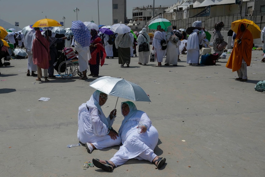 Two Muslim women take shade under an umbrella. 
