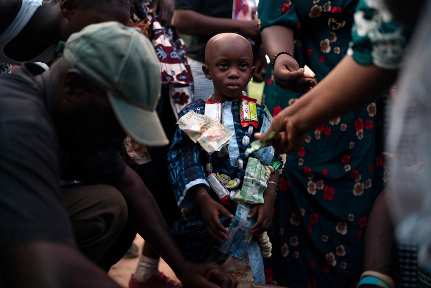 a young boy in a colourful outfit is surrounded by adults 