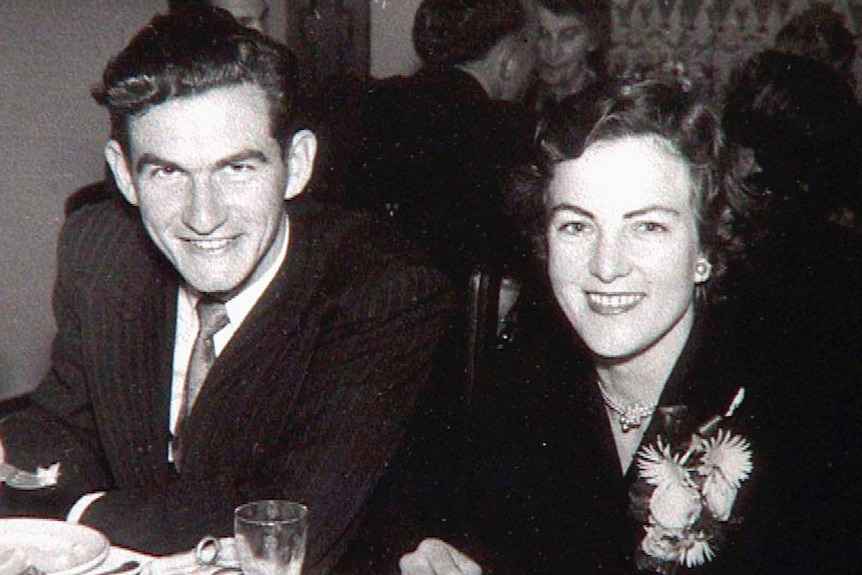 A black and white photo showing a young couple, seated, smiling at the camera.