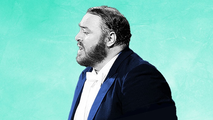 A black-and-white photograph of Luciano Pavarotti, facing the left wearing a dark blue jacket on a cyan background.