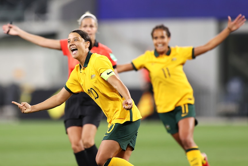 Sam Kerr runs with her arms pointing out to her side and Mary Fowler running behind her