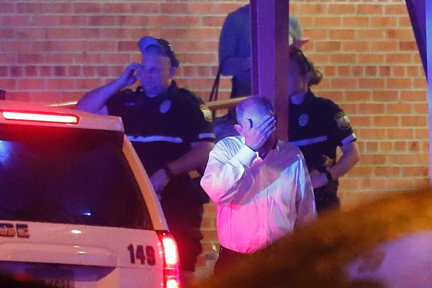 A man surrounded by police puts his hand over his face.