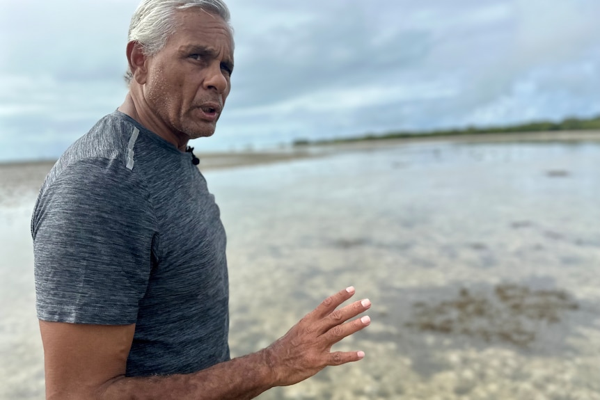 Indigenous man in a grey shirt standing near wetlands.