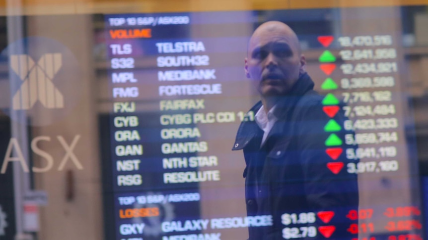 An investor is reflected in a window displaying a board showing stock prices