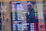 An investor is reflected in a window displaying a board showing stock prices