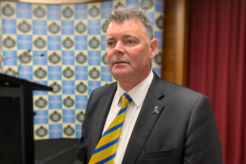 A man wearing a suit in front of a banner and a curtain