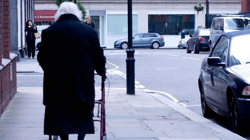 An elderly woman walks up a street with the help of a zimmer frame