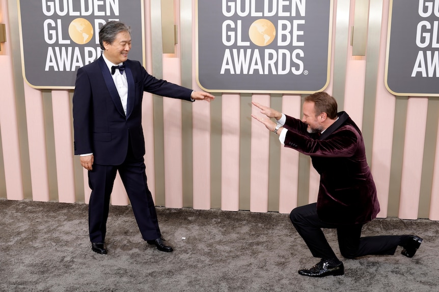 Rian Johnson bows down to Park Chan-wook on the Golden Globes red carpet. Park has his arm outstretched and smiles brightly.
