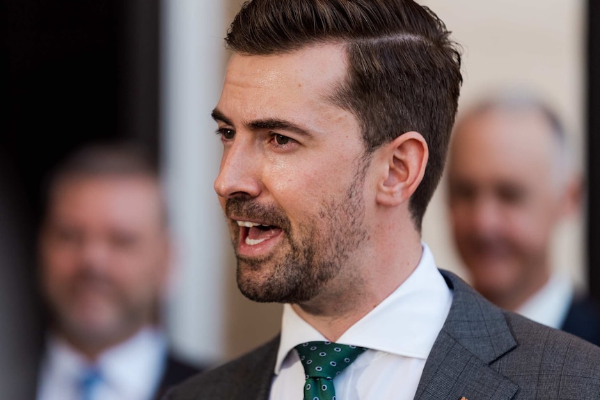 A side profile of Zak Kirkup speaking at a press conference