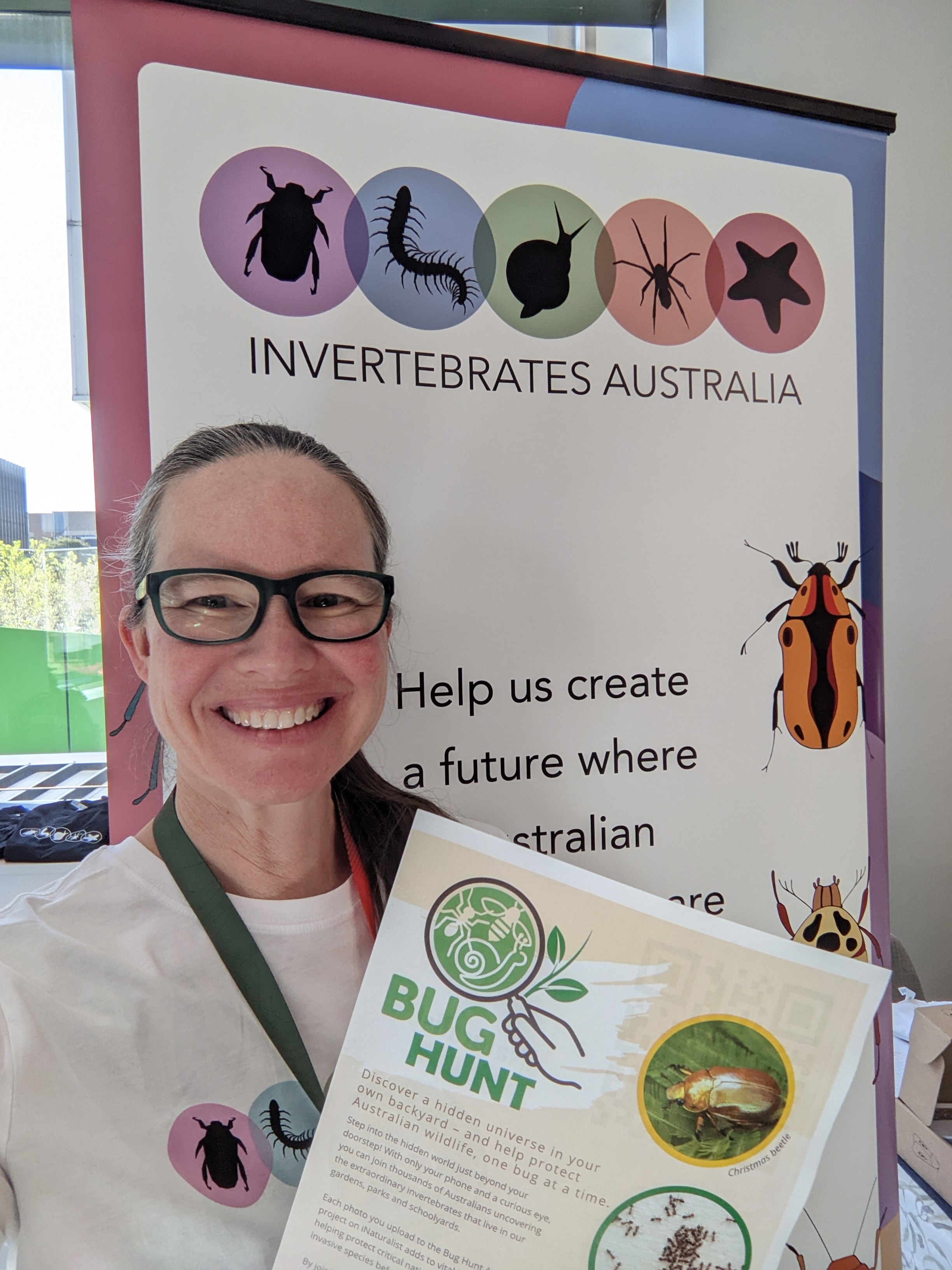 Uma mulher de óculos sorrindo e segurando uma placa com o título 