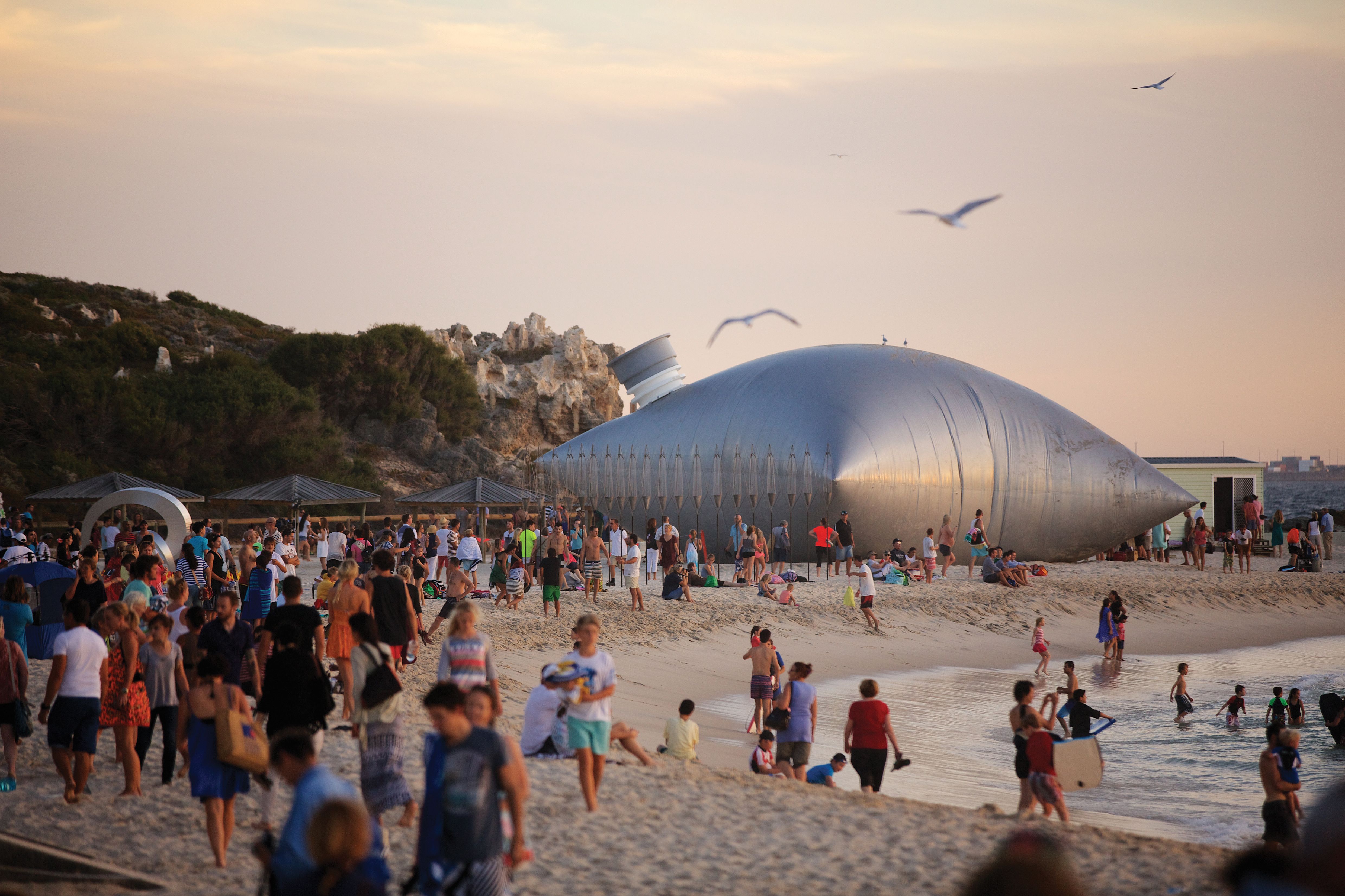 A large sculpture of a cask wine bag sits on a busy beach.