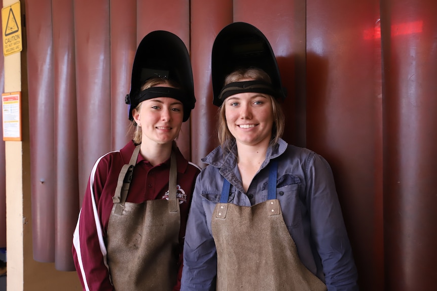 Two women with leather aprons and welding masks.